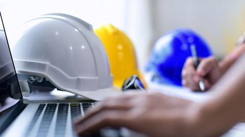 Person typing on a laptop with construction hard hats next to them.